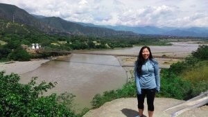 girl standing on a hill with a river and bridge built by a drunk engineer in the background