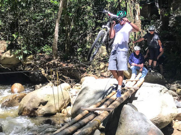 man crossing bamboo bridge carrying bike