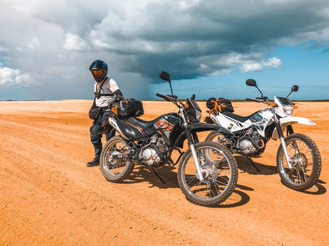 man standing by two enduro bikes in the desert